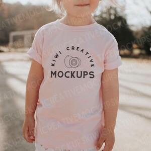 Puede incluir: Una camiseta rosa para ni&ntilde;os peque&ntilde;os con un gr&aacute;fico negro de un kiwi y el texto "Kiwi Creative Mockups".
