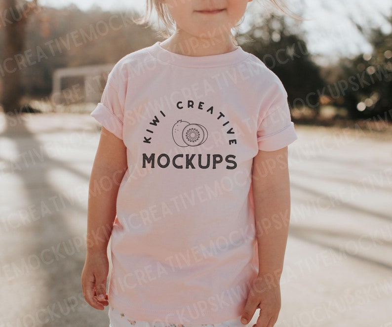 Puede incluir: Una camiseta rosa para ni&ntilde;os peque&ntilde;os con un gr&aacute;fico negro de un kiwi y el texto "Kiwi Creative Mockups".