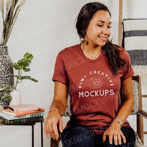 May include: A woman wearing a maroon t-shirt with the text "Kiwi Creative Mockups" in white. The shirt has a graphic of two kiwi fruits.