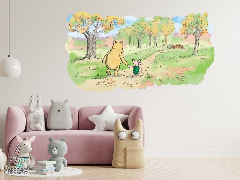 May include: A Winnie the Pooh and Piglet wall decal featuring the two characters walking hand-in-hand along a forest path. The decal is set against a white wall with a pink sofa and plush toys in the foreground.