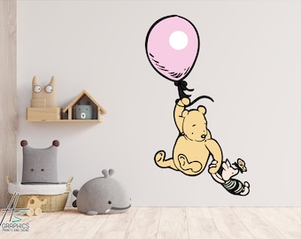 May include: A Winnie the Pooh wall decal featuring Winnie the Pooh holding onto a pink balloon with a black string. Piglet is holding onto Winnie the Pooh's arm. The decal is on a white wall.