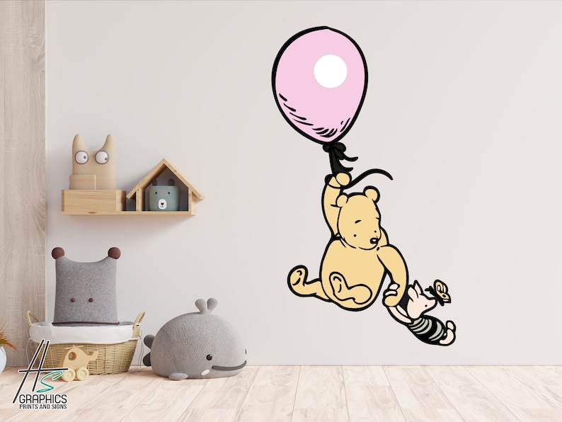 Puede incluir: Una calcoman&iacute;a de pared de Winnie the Pooh con Winnie the Pooh sujetando un globo rosa con una cuerda negra. Piglet se agarra al brazo de Winnie the Pooh. La calcoman&iacute;a est&aacute; en una pared blanca.
