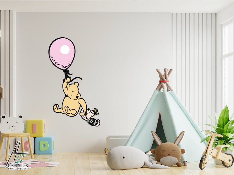 Puede incluir: Una calcoman&iacute;a de pared de Winnie de Pooh y Piglet con Winnie de Pooh sosteniendo un globo rosa y Piglet alcanz&aacute;ndolo. La calcoman&iacute;a est&aacute; en una pared blanca en una guarder&iacute;a con una tienda de campa&ntilde;a tipi, un juguete de madera y una planta.