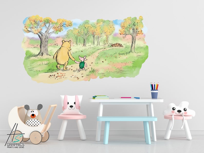 May include: A Winnie the Pooh and Piglet wall decal featuring a watercolour illustration of the characters walking down a path in a forest. The decal is displayed on a white wall in a child's room with a white table, blue bench, and pink chair.
