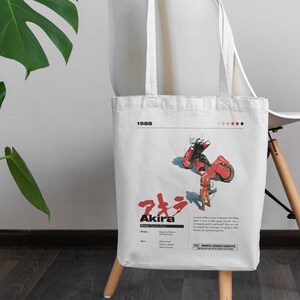 May include: A white tote bag with a red and black illustration of a motorcycle and a person. The bag has the text "Akira" and "1988" printed on it. The text "Parental Guidance Suggested" is also printed on the bag.