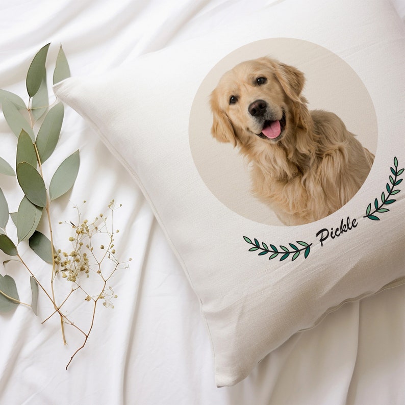 May include: A white pillow with a round image of a golden retriever dog with the name "Pickle" written below the image. The image is surrounded by green leafy branches.