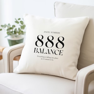 May include: White throw pillow with black text that reads "ANGEL NUMBERS 888 BALANCE Everything is falling into place as it's meant to be."