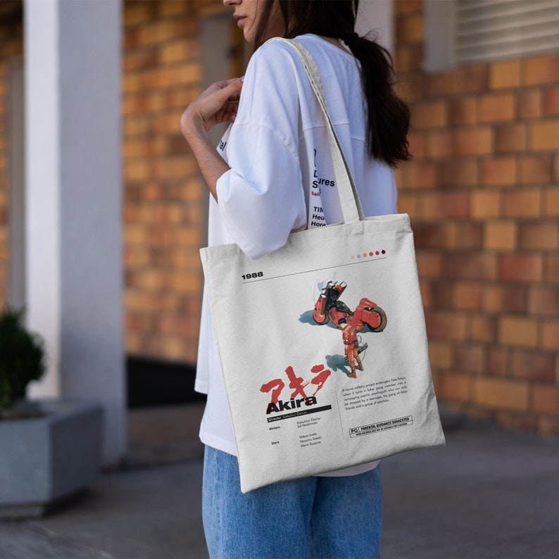 May include: A white tote bag with a red and black illustration of a character riding a motorcycle. The bag has the text "Akira" and "1988" printed on it.