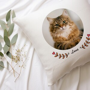 May include: A white pillow with a round image of a brown tabby cat with green eyes. The image is surrounded by a floral design with red hearts and the name "Luna" written in cursive.