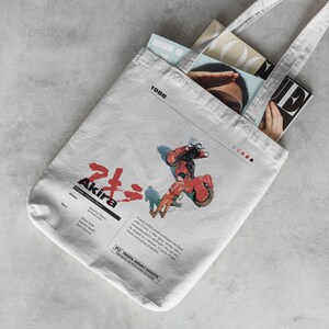May include: White tote bag with a red and black illustration of a motorcycle and a person riding it. The bag has the text "Akira" and "1988" printed on it.