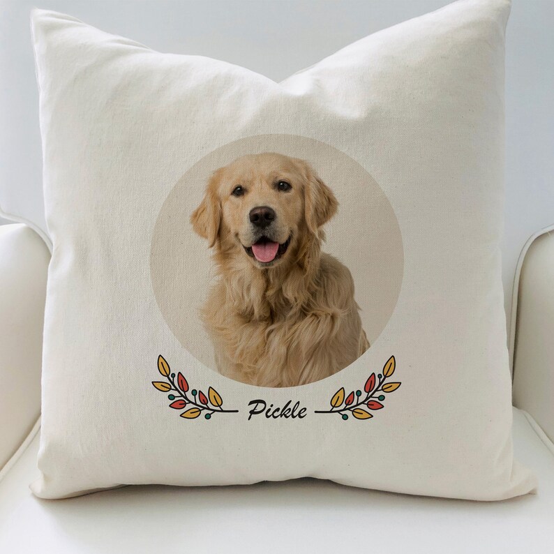 May include: A white pillow with a round image of a golden retriever dog with the name "Pickle" written below the image. The image is surrounded by a wreath of orange, red, and yellow leaves.