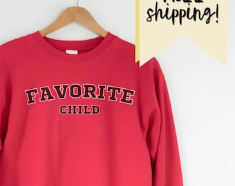 May include: Red sweatshirt with the text "FAVORITE CHILD" in black lettering.
