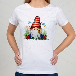 May include: White t-shirt with a graphic of a gnome wearing a red, white, and blue hat with a peace sign. The gnome is sitting in a field of flowers and butterflies.
