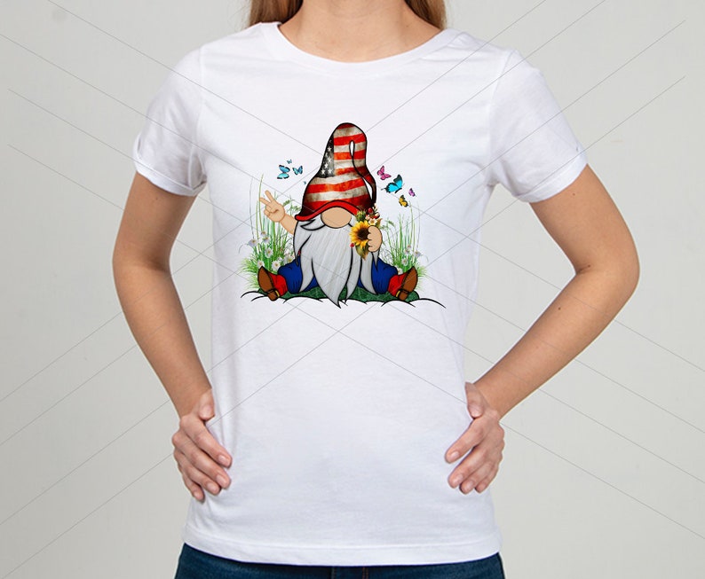 May include: White t-shirt with a graphic of a gnome wearing a red, white, and blue hat with a peace sign. The gnome is sitting in a field of flowers and butterflies.