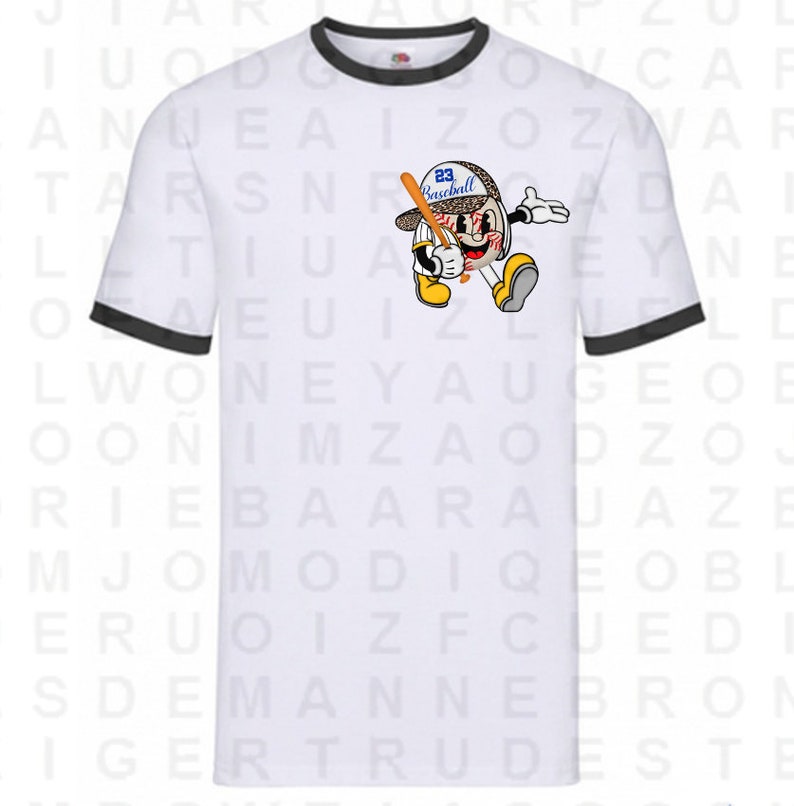 Peut inclure: T-shirt blanc avec bordure noire en c&ocirc;tes, repr&eacute;sentant un personnage de dessin anim&eacute; de baseball portant un chapeau avec le num&eacute;ro 23 et le mot "Baseball" dessus. Le personnage tient une batte et a une expression surprise. L'arri&egrave;re-plan du t-shirt est recouvert d'un motif al&eacute;atoire de lettres.