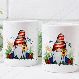 May include: Two white ceramic mugs with a design of a gnome wearing a red, white, and blue hat and holding a sunflower. The gnome is sitting on a bed of green grass with butterflies flying around.