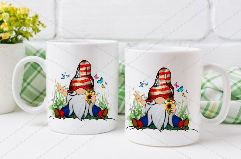 May include: Two white ceramic mugs with a design of a gnome wearing a red, white, and blue hat and holding a sunflower. The gnome is sitting on a bed of green grass with butterflies flying around.