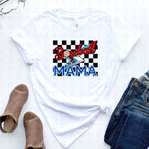 Peut inclure: T-shirt blanc avec un fond &agrave; carreaux noirs et blancs, une balle de baseball rouge avec un &eacute;clair et les mots "Baseball Mama" en bleu.