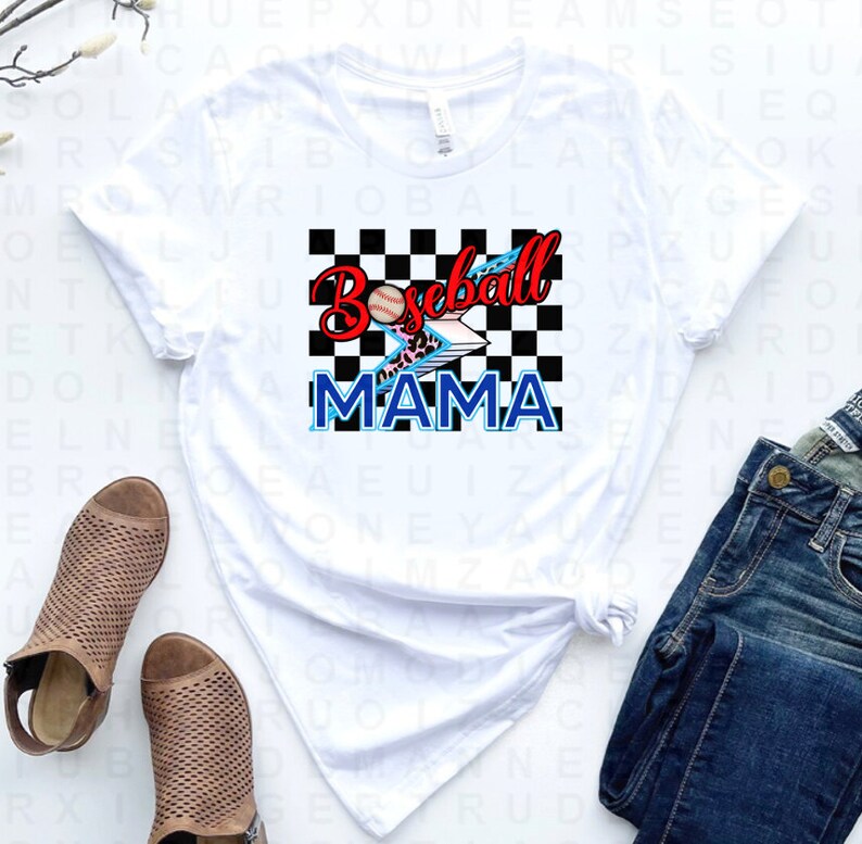 Peut inclure: T-shirt blanc avec un fond &agrave; carreaux noirs et blancs, une balle de baseball rouge avec un &eacute;clair et les mots "Baseball Mama" en bleu.
