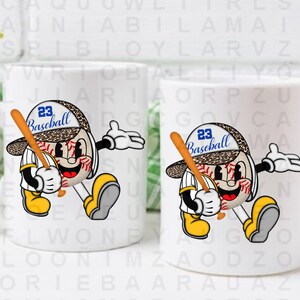 Peut inclure: Deux tasses en c&eacute;ramique blanche avec un motif sur le th&egrave;me du baseball. Le motif repr&eacute;sente un ballon de baseball de dessin anim&eacute; avec un visage, portant un chapeau qui dit "23 Baseball".