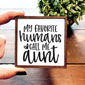 May include: White wooden sign with brown frame, featuring the text "My favorite humans call me aunt" in black cursive font.