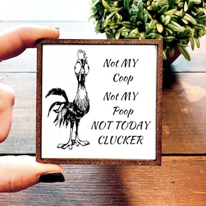 May include: A white wooden sign with a brown frame features a black and white cartoon rooster with the text "Not MY Coop Not MY Poop NOT TODAY CLUCKER".