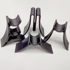 May include: Four black plastic stands for displaying items. The stands are made of a flexible material and have a curved design. The stands are different sizes and heights.