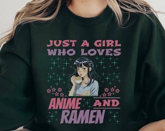 May include: A dark green sweatshirt with the text "Just a girl who loves anime and ramen" in pink and purple lettering. The text is surrounded by small pink flowers and green stars. A cartoon anime girl is holding a bowl of ramen in the center of the design.
