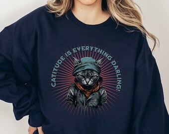 May include: A navy blue sweatshirt with a graphic of a cat wearing a bandana and a hat. The text "Catitude is everything darling!" is printed on the sweatshirt.