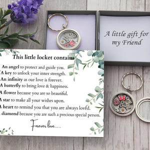 May include: A silver locket with a clear glass front, containing charms including a pink butterfly and a flower, presented in a grey gift box. The box includes a card with text about the locket's meaning. The text "A little gift for my Friend" is also visible.