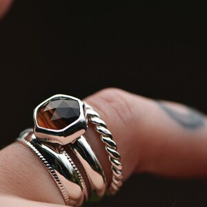 May include: A silver ring with a faceted brown gemstone, worn with three other silver bands.