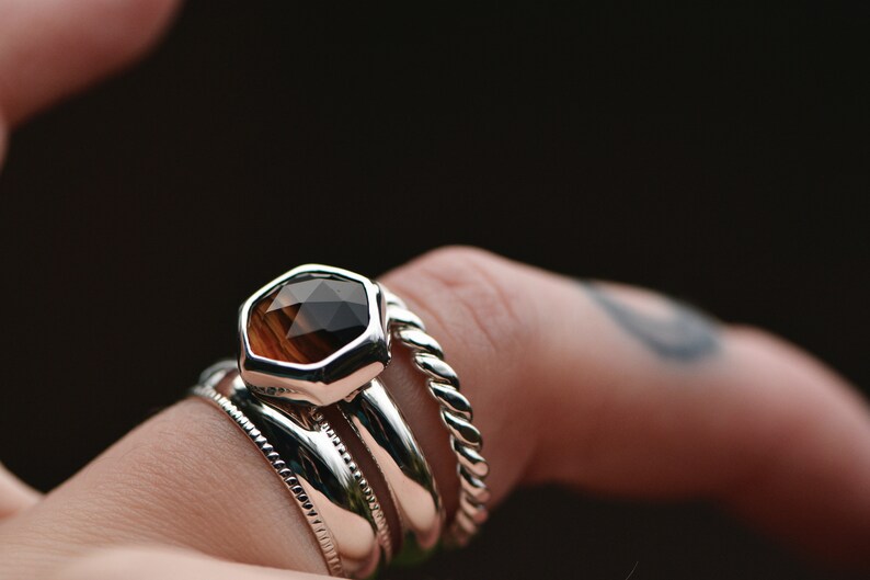 May include: A silver ring with a faceted brown gemstone, worn with three other silver bands.