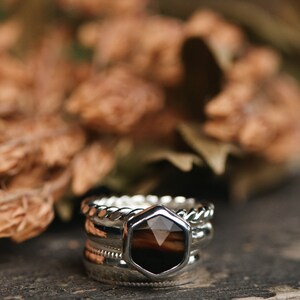 May include: A set of four silver rings with a hexagonal brown gemstone in the center. The rings are stacked on top of each other and have different textures.