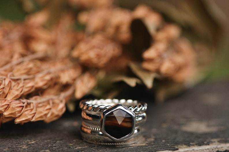 May include: A set of four silver rings with a hexagonal brown gemstone in the center. The rings are stacked on top of each other and have different textures.