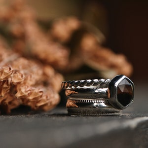 May include: A set of three silver rings with a dark brown gemstone in a hexagonal setting. The rings are stacked on top of each other.