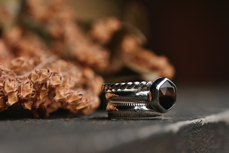 May include: A set of three silver rings with a dark brown gemstone in a hexagonal setting. The rings are stacked on top of each other.