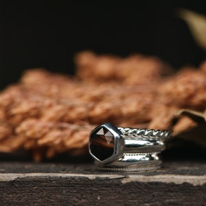 May include: A set of three silver rings with a brown gemstone in the center ring. The rings are stacked on a wooden surface.