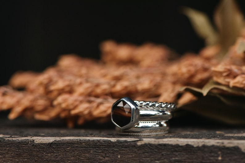 May include: A set of three silver rings with a brown gemstone in the center ring. The rings are stacked on a wooden surface.