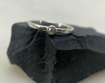 May include: A silver ring with a single, round, clear gemstone set in the center.