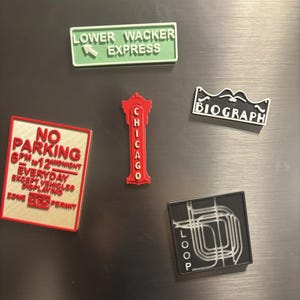 Op de afbeelding: Een verzameling van vijf magneten met verschillende ontwerpen met als thema Chicago. De magneten zijn rood, zwart, wit en groen. De magneten bevatten de tekst "Lower Wacker Express", "No Parking 6PM to 12 Midnight Everyday Except Vehicles Displaying Zone 363 Permit", "Biograph", "Chicago" en "Loop".