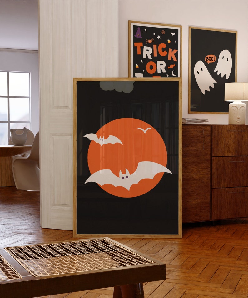 A gallery wall set of 3 framed Halloween artworks in orange, black and white color schemes.