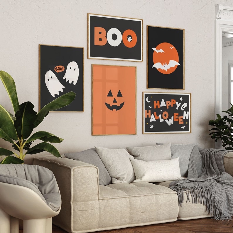 A gallery wall set of 5 framed Halloween artworks in orange, black and white color schemes above a couch.