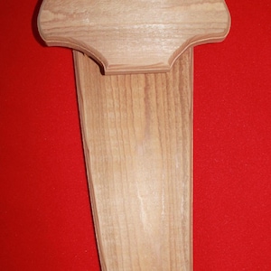 May include: A wooden wall mount plaque with a rounded top and a long, narrow base. The plaque is made of light-colored wood with a natural grain pattern.