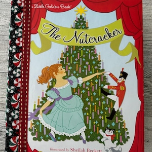 Puede incluir: Un libro de Little Golden Book titulado "The Nutcracker" con ilustraciones de Sheilah Beckett. La portada presenta una bailarina con un vestido azul, un cascanueces y un árbol de Navidad. El lomo tiene un patrón de bastones de caramelo en blanco y negro.