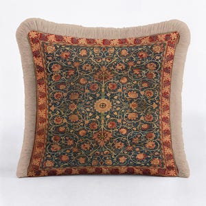 May include: A square throw pillow featuring a dark blue central panel with an intricate floral and vine pattern in shades of orange, red, and gold. The pillow is framed by a decorative red border and finished with a thick, beige fringe trim.
