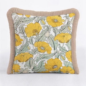 May include: A square throw cushion featuring a white background with a repeating pattern of yellow poppy flowers and sage green foliage. The cushion is finished with a textured, light beige fringe trim along all four edges of the square cushion.