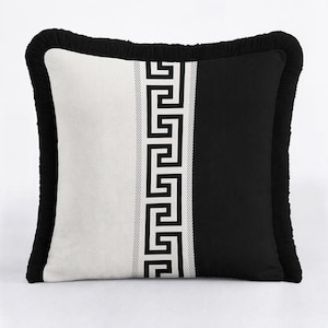 May include: A square throw pillow featuring a split design with a white left side and a black right side. A central vertical band displays a black and white Greek key pattern. The entire pillow is finished with a black ruffled fringe border.