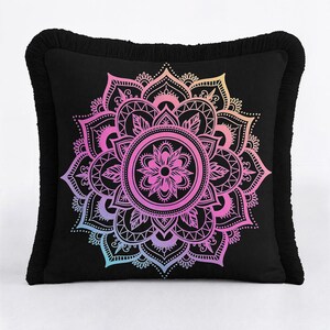 May include: A square black throw pillow featuring a central mandala design with a gradient of colors transitioning from orange and pink at the top to purple and blue at the bottom. The pillow is finished with a black fringe trim along all four edges.