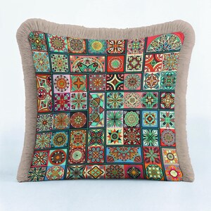 May include: A square throw pillow featuring a vibrant patchwork design of various colorful mandala patterns in shades of red, blue, green, and orange. The pillow is finished with a thick, textured beige fringe border along all four edges.