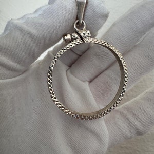Puede incluir: Pendiente de moneda de plata con un dise&ntilde;o texturizado en forma de diamante. El pendiente tiene un bucle en la parte superior para sujetarlo a una cadena.